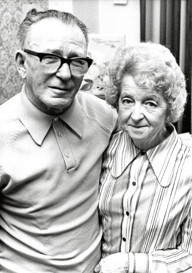 An elderly couple smiling at the camera on their golden wedding