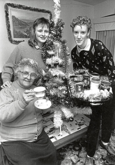 Oldmachar Academy Aberdeen pupils gather around a table-top christmas tree with trays of food in their hands as an elderly woman drinks a cup of tea