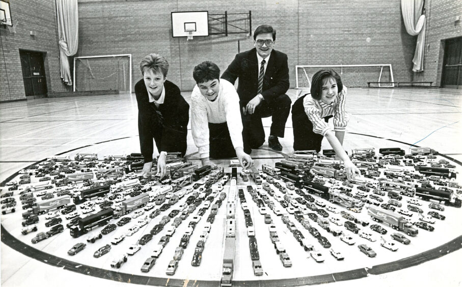 Four students surrounded by rows of toy cars