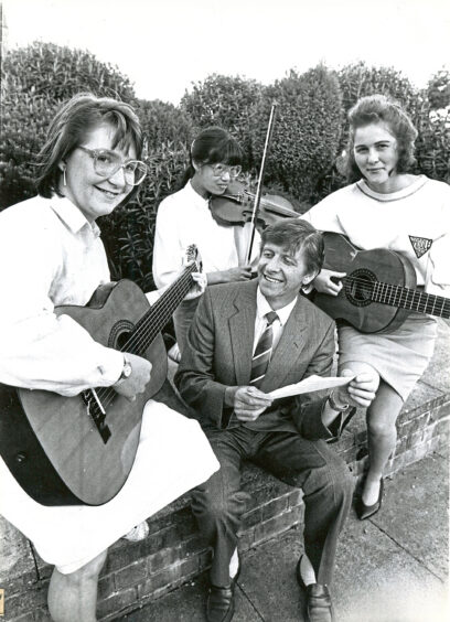 A man in a suit sits among three oldmachar academy aberdeen students with string instruments