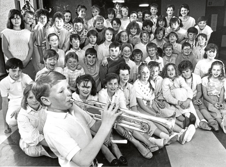 A boy plays the trumpet at the front of a large group of students