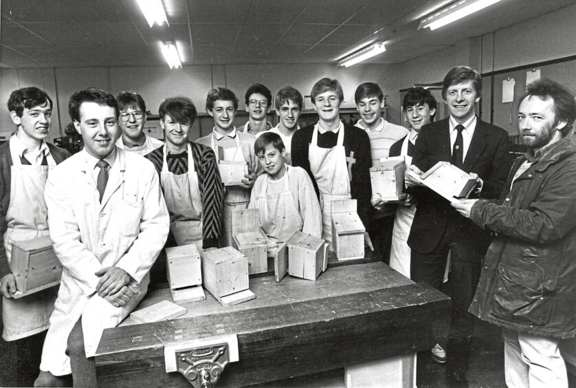 A group of Oldmachar academy Aberdeen pupils gathered around a table with wooden bat-boxes on it, on the right is an Aberdeen University research student
