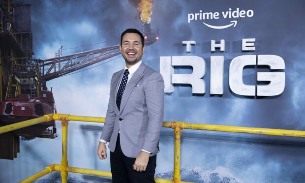 Martin Compston smiles on the red carpet, with a large poster for The Rig in the background.