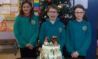 Crossroads Primary P6 pupils Elana Myatt, Dylan Macdonald and Moira Darby admire the cake gifted by King Charles III. Image: Iain Grant
