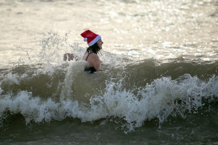 A person with a Christmas hat dipping in the sea.