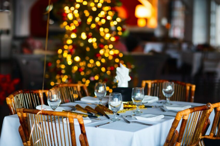 A table set for a Christmas meal with a Christmas tree in the background.