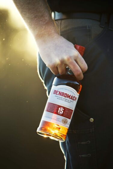 A man holding a bottle of Benromach 15 Year Old