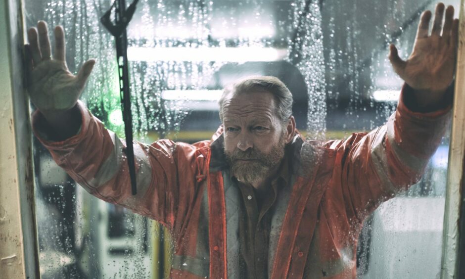 Iain Glen leans on a foggy window in a high-vis jacket in a still from Prime's The Rig