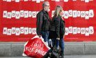 Two people with shopping bags walk past a shop window with 'reductions' signs