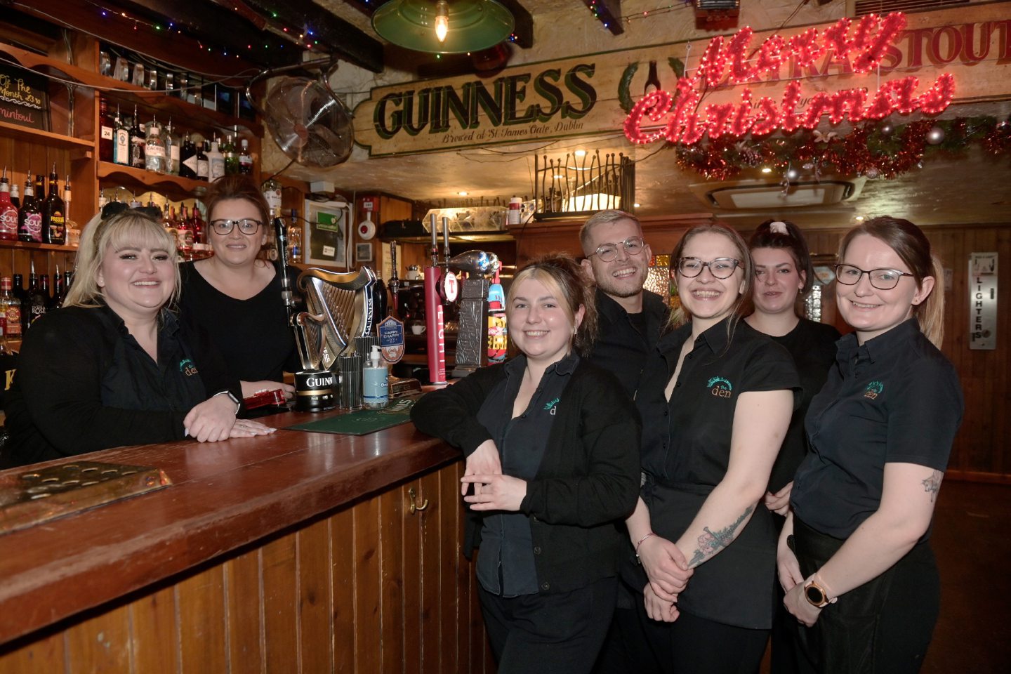 The bar staff from Johnny Foxes standing in front of and behind the bar, which has a large Guinness tap with a silver harp on it