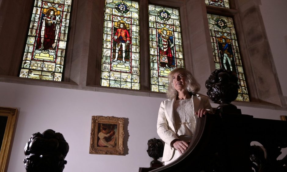 A woman dressed in white at the top of the stairs with stained glass windows behind