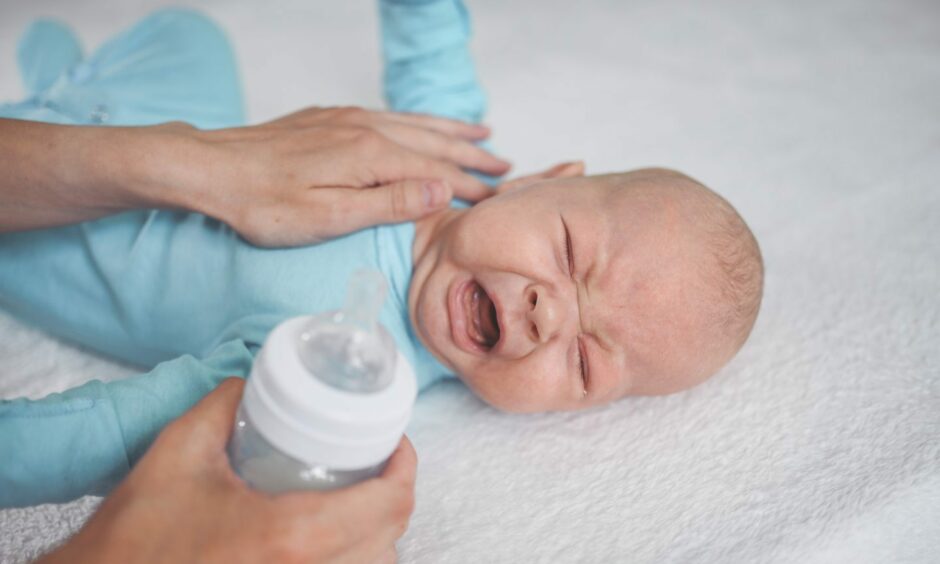 A crying baby who is being soothed and offered a bottle.