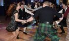 A group of people holding hands and ceilidh dancing.