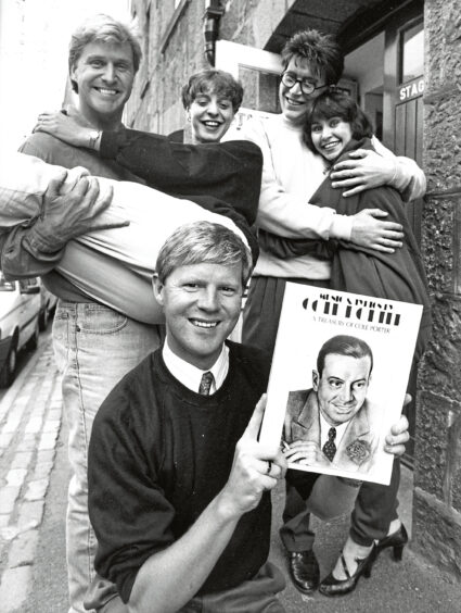 Actors embracing while one actor holds up a program for their show