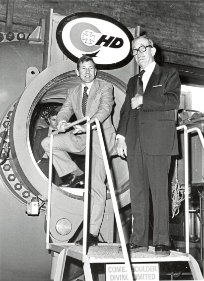 Two men in suits next to a hydrolic chamber at the base of Aberdeen oil company Comex