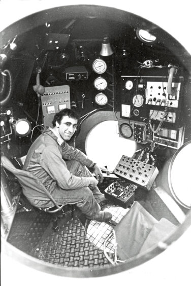 A man inside the Comex observation bell, sat in front of a control panel