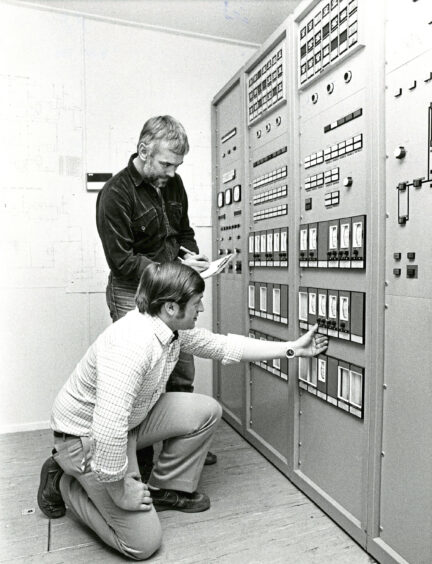 Two men looking at a wall of meters and controls that are used for aberdeen oil workers training