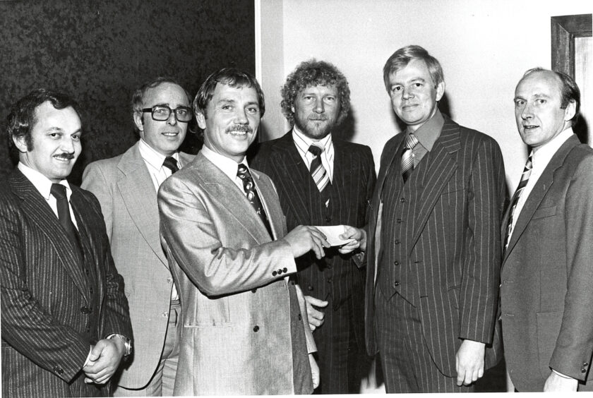 A group of six men in suits smiling at the camera. One of the men is handing the man at the front a certificate