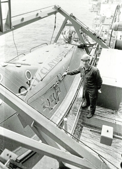 An aberdeen oil safety officer standing next to a lifeboat
