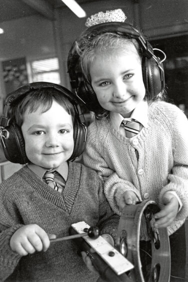 A girl and boy, both five years old, wear headphones while holding a xylophone and tamborine