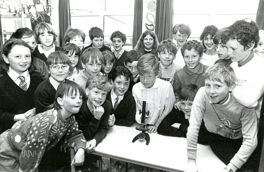 Kaimhill school pupils in science class, surrounding a table with a microscope on it 