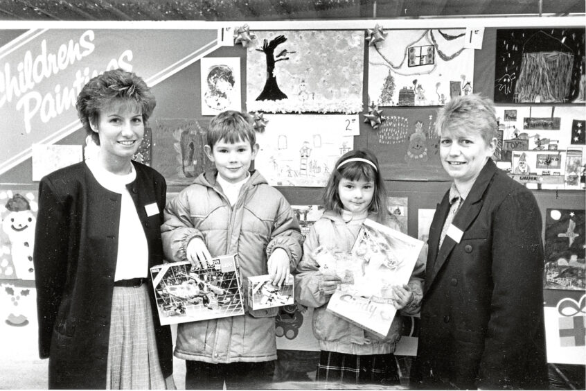 Two members of Asda staff stand next to a girl and boy who are holding their prizes for winning the competition