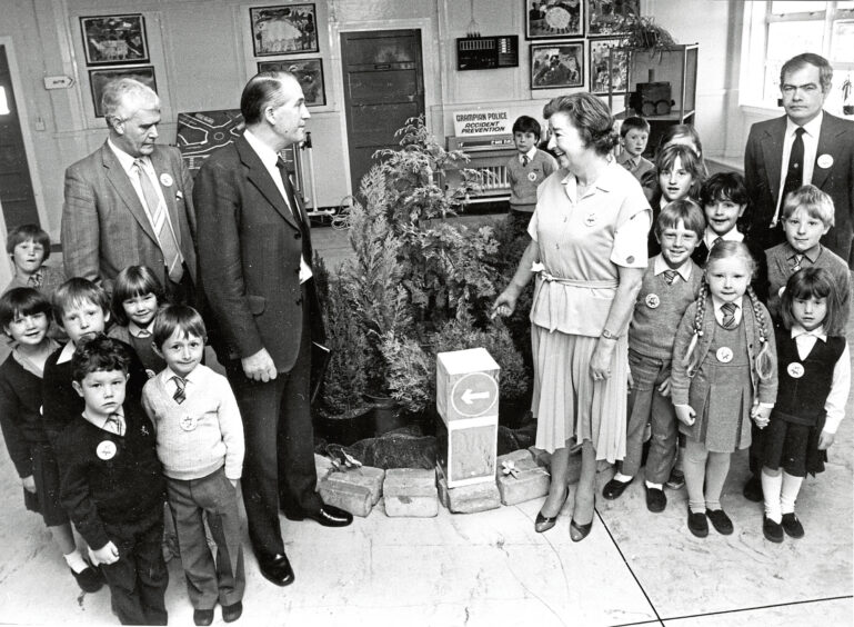 the headteacher, policemen and a group of children gather around a small roundabout in the entrance hall