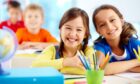 two girls smile while sitting at desk with art materials