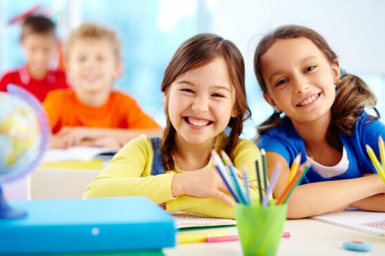 two girls smile while sitting at desk with art materials