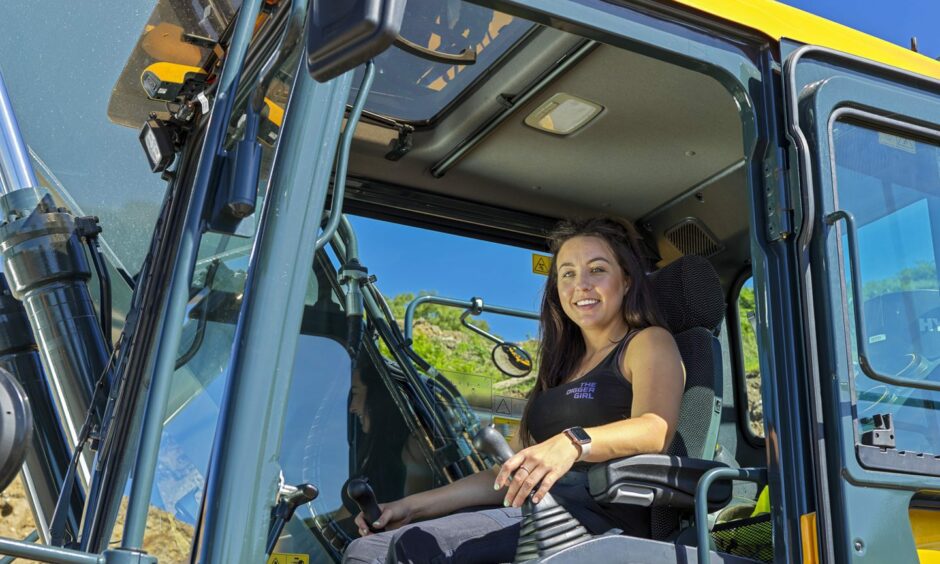 Digger Girl Amy Underwood smiling from the cab of a digger. 