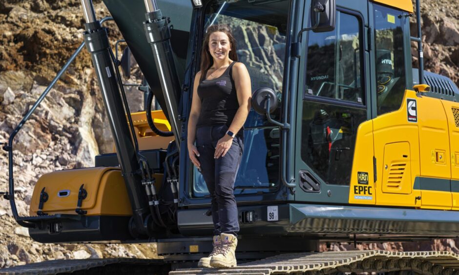 Amy stands in front of a digger. 