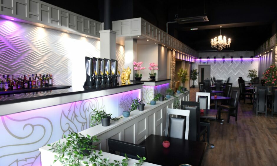 Inside Kin Kao in Aberdeen, featuring white walls and a white bar with grey dragons art painted on. There are black chairs and tables in the dining area. There are purple lights under the bar and along the walls
