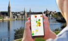 A pair of hands holding a mobile phone with a map of Inverness on the screen. The Inverenss river view is in the background.