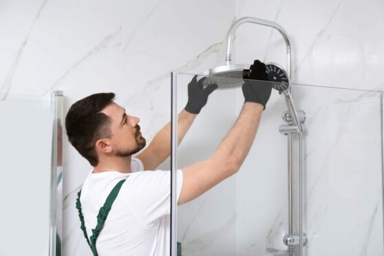 A bathroom fitter fixing a showerhead. Claude's Tradesmen are expert kitchen and bathroom renovators.