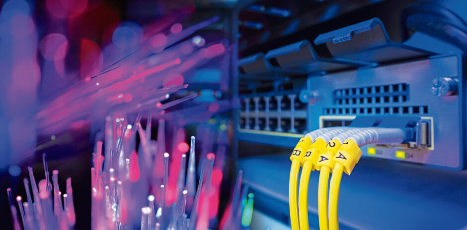 Yellow fiber optic cable with lighting of fiber optics and high speed network router switch in a technology data center room.