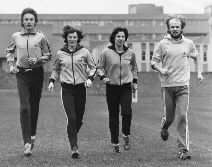 Four people running in a row and smiling at the camera