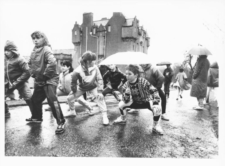 A group of young girls squatting and stretching in preparation for the upcoming race. One of the girls is holding an umbrella
