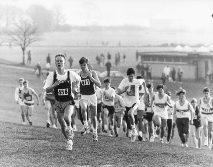 A boy runs at the front of a group of young men at a cross country running championship in the north-east