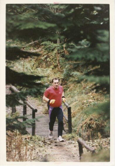 A man runs across a wooden bridge in a woodland area