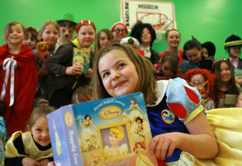 A girl dressed as snow white with her disney princess storybook in front of her with a group of children in costumes behind her