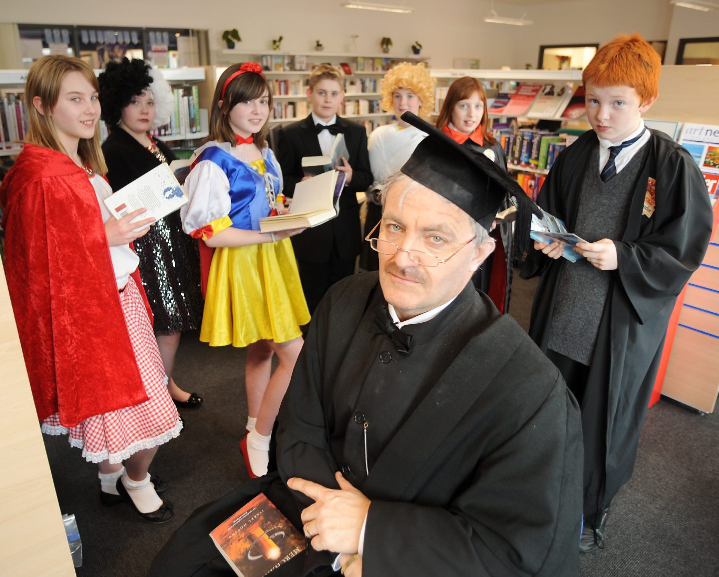 School pupils in costumes in the school library with their teacher for world book day