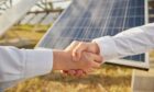 Business men shaking hands on a deal at a solar farm.