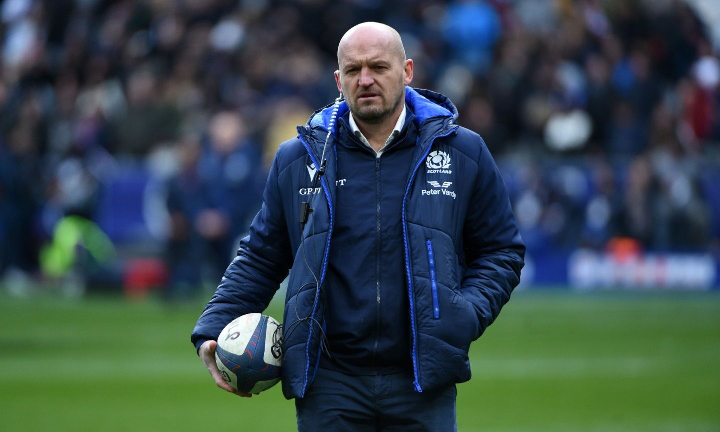 Gregor Townsend on a sportsfield holding a rugby ball under his arm walking towards camera. 
