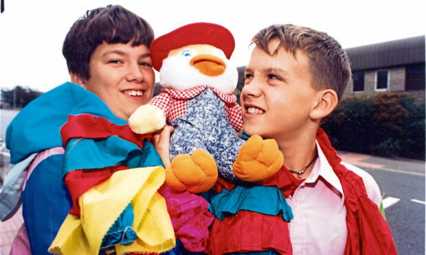 Two boys with the Gang Show mascot between them on their shoulders.
