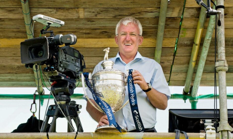 Hugh Dan MacLennan holding the cup behind a film camera