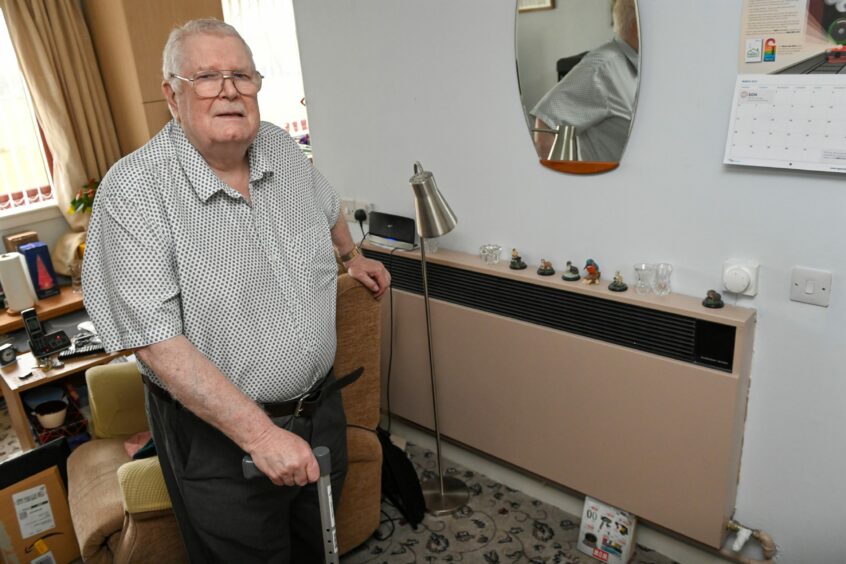 Ken Campbell stands in front of his heater in Blackhills Court sheltered housing.