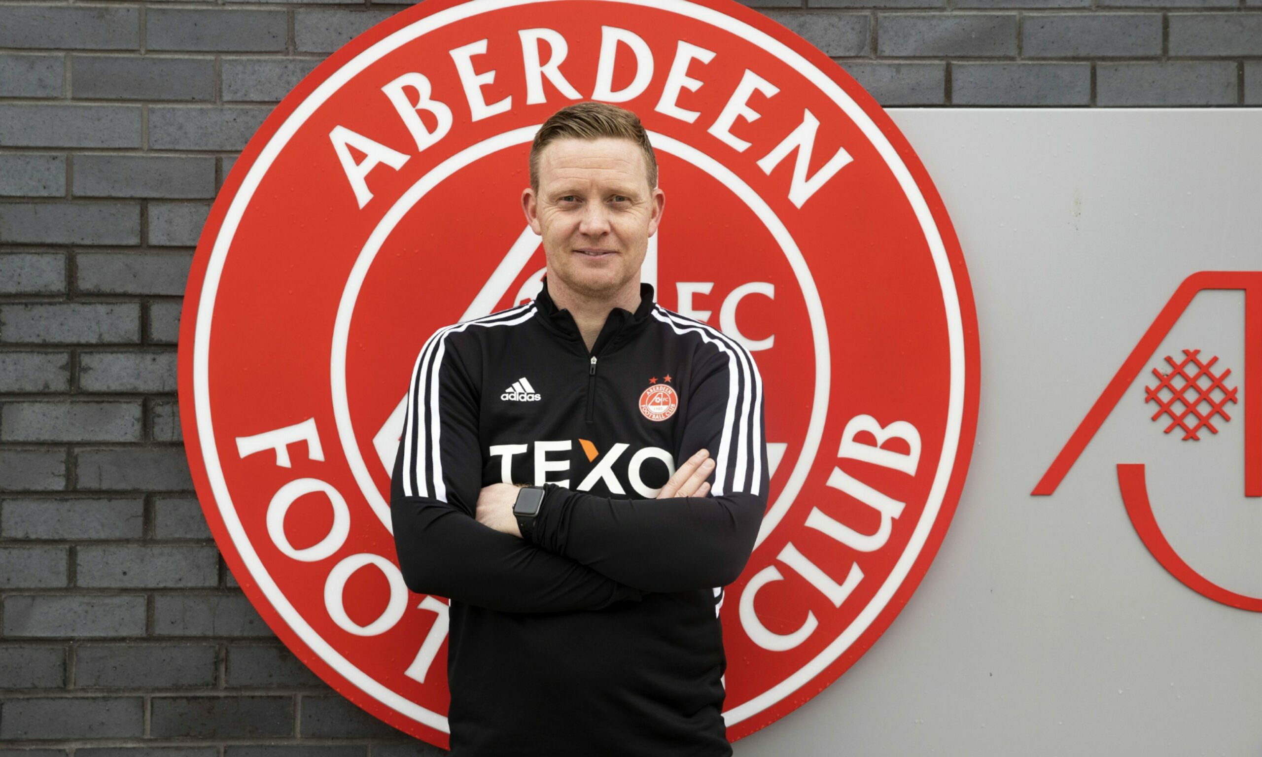 Barry Robson standing in front of the Aberdeen badge at the club's Cormack Park training ground.