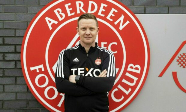 Barry Robson standing in front of the Aberdeen badge at the club's Cormack Park training ground. Photo SNS