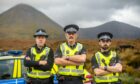 Three police officers with arms crossed and high-viz vests on, with hills in the background