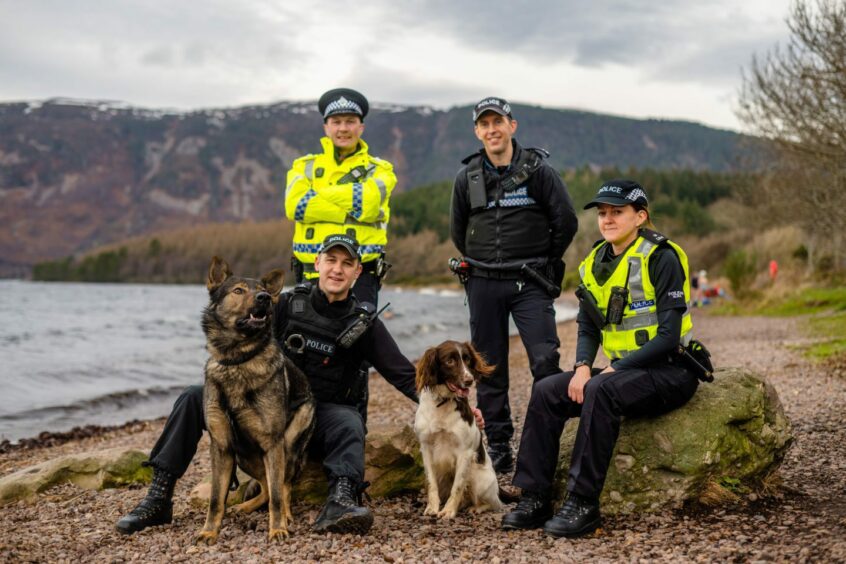 Four police officers with two police dogs on the shores of a loch